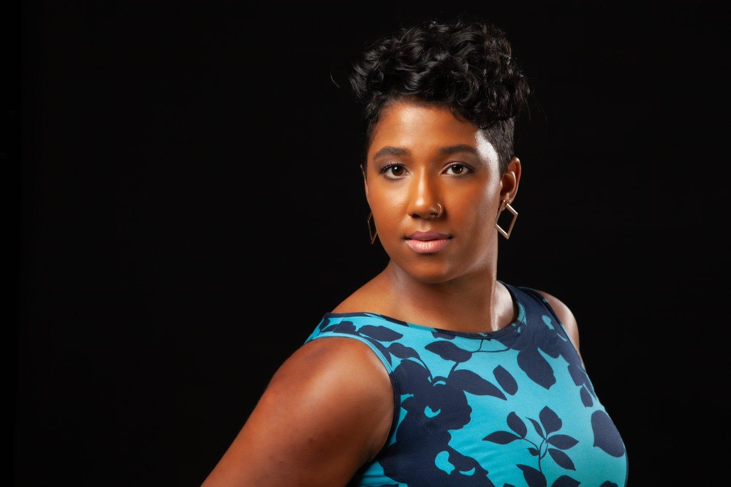 Rhyana looking towards camera in a blue and black floral dress.