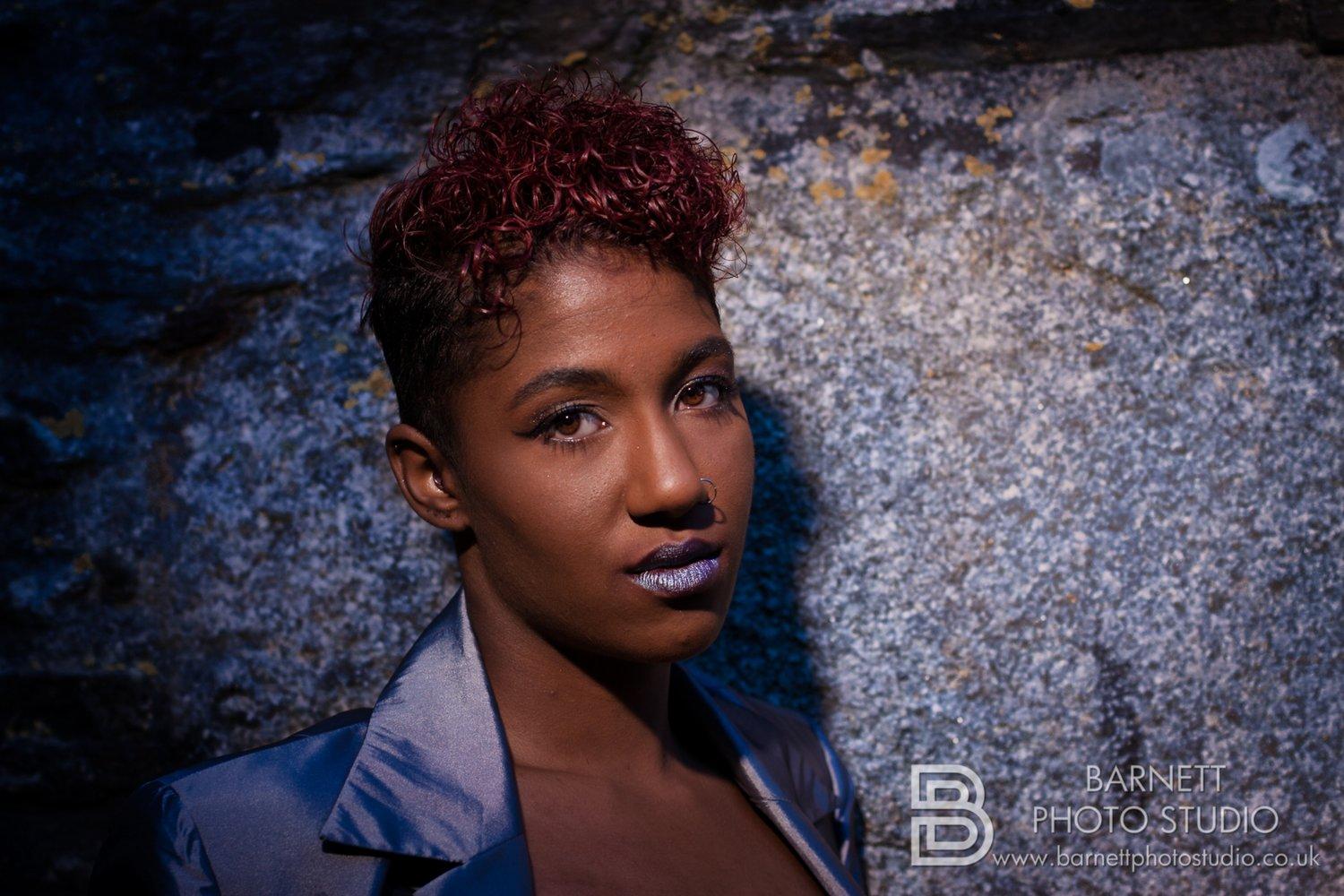 Close up of Rhyana in a grey satin suit, looking towards the camera.