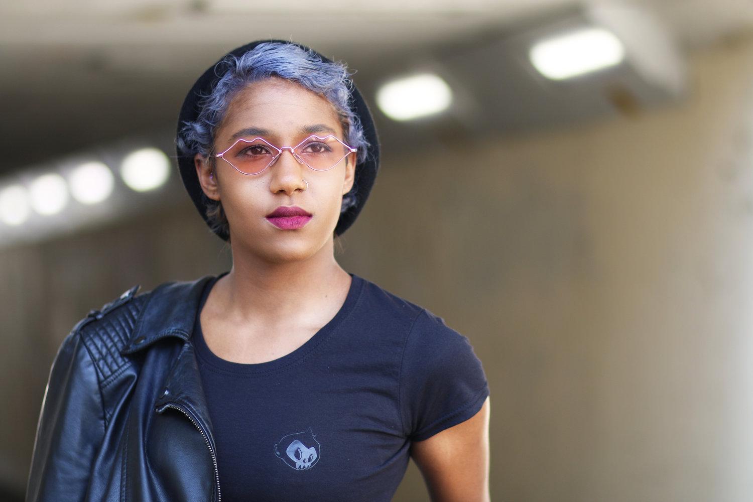 Rhyana with a black leather jacket on one shoulder, wearing a dark blue t-shirt and black beanie.