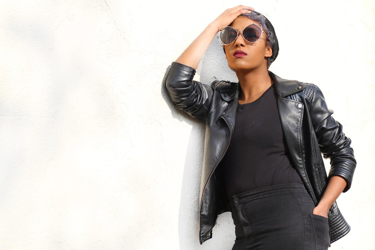 Rhyana against a white background, wearing a black leather jacket, sunglasses and dark blue t-shirt.