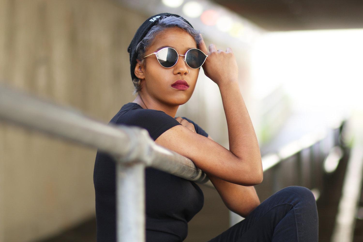 Rhyana sat through the bars of a raliing, leaning against one arm and looking towards the camera.