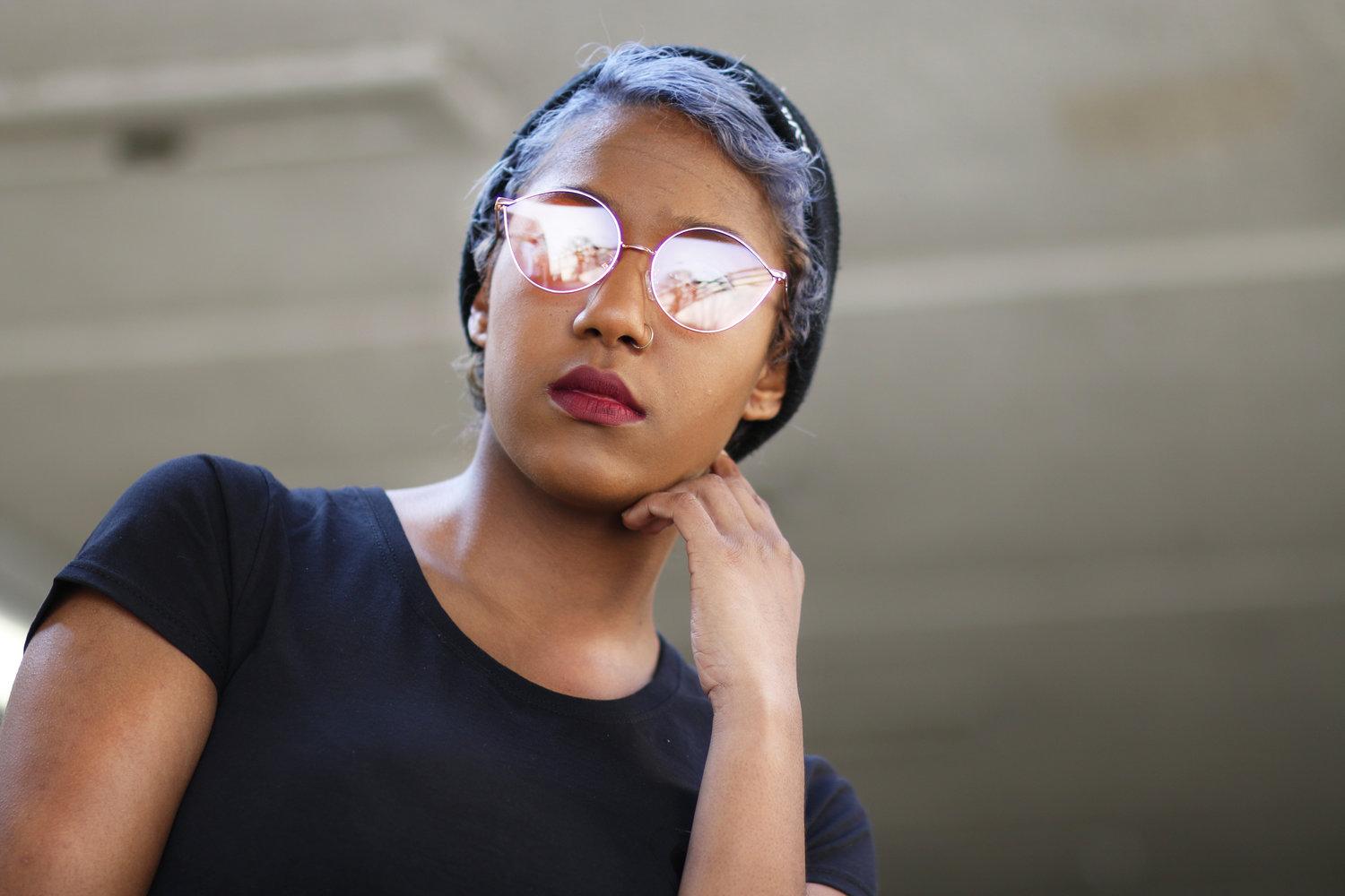 Rhyana leaning on one hand, looking at the camera through reflective sunglasses.