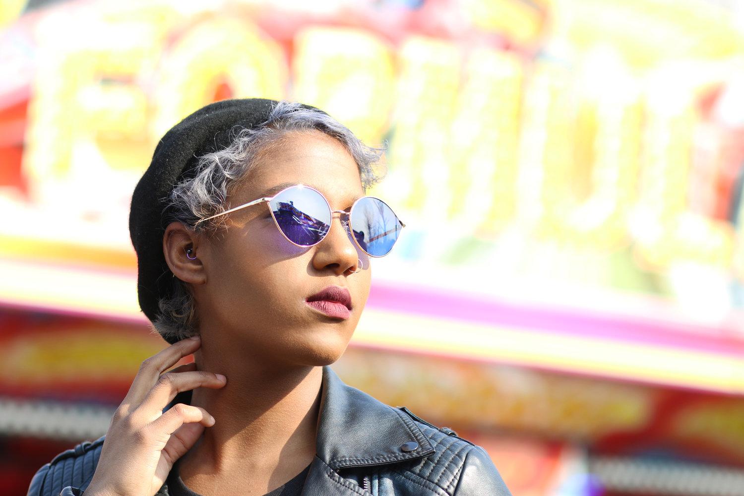 Rhyana in a black leather jacket, looking off-camera against a blurred colourful background.