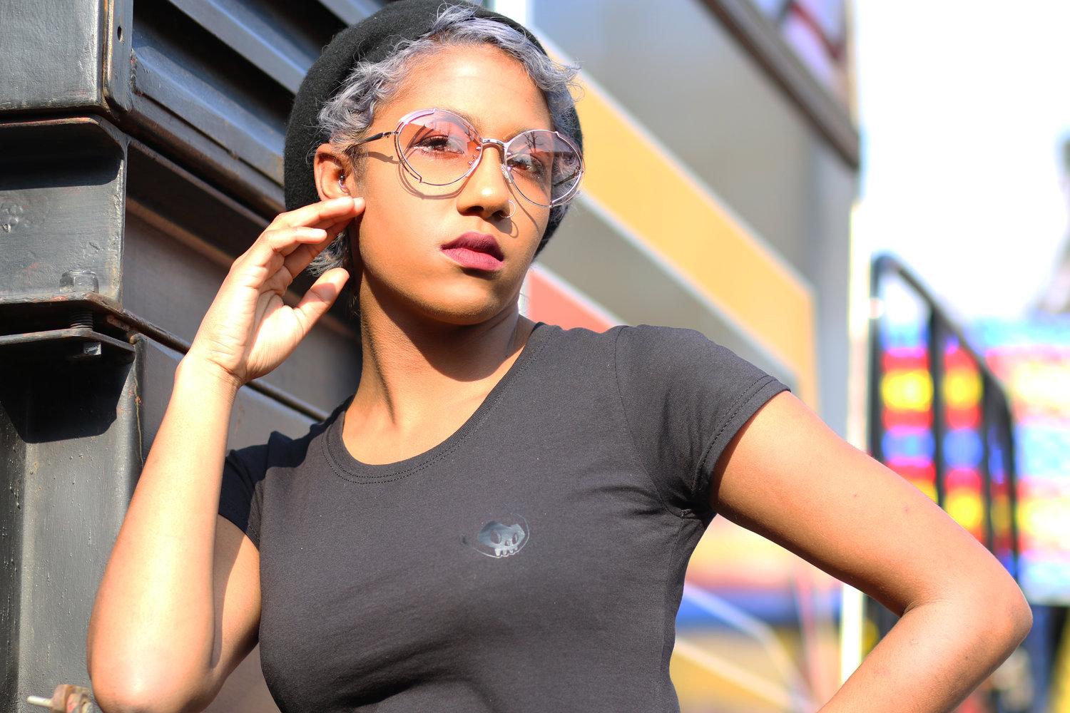 Rhyana leaning against one hand, looking towards camera through rose sunglasses.