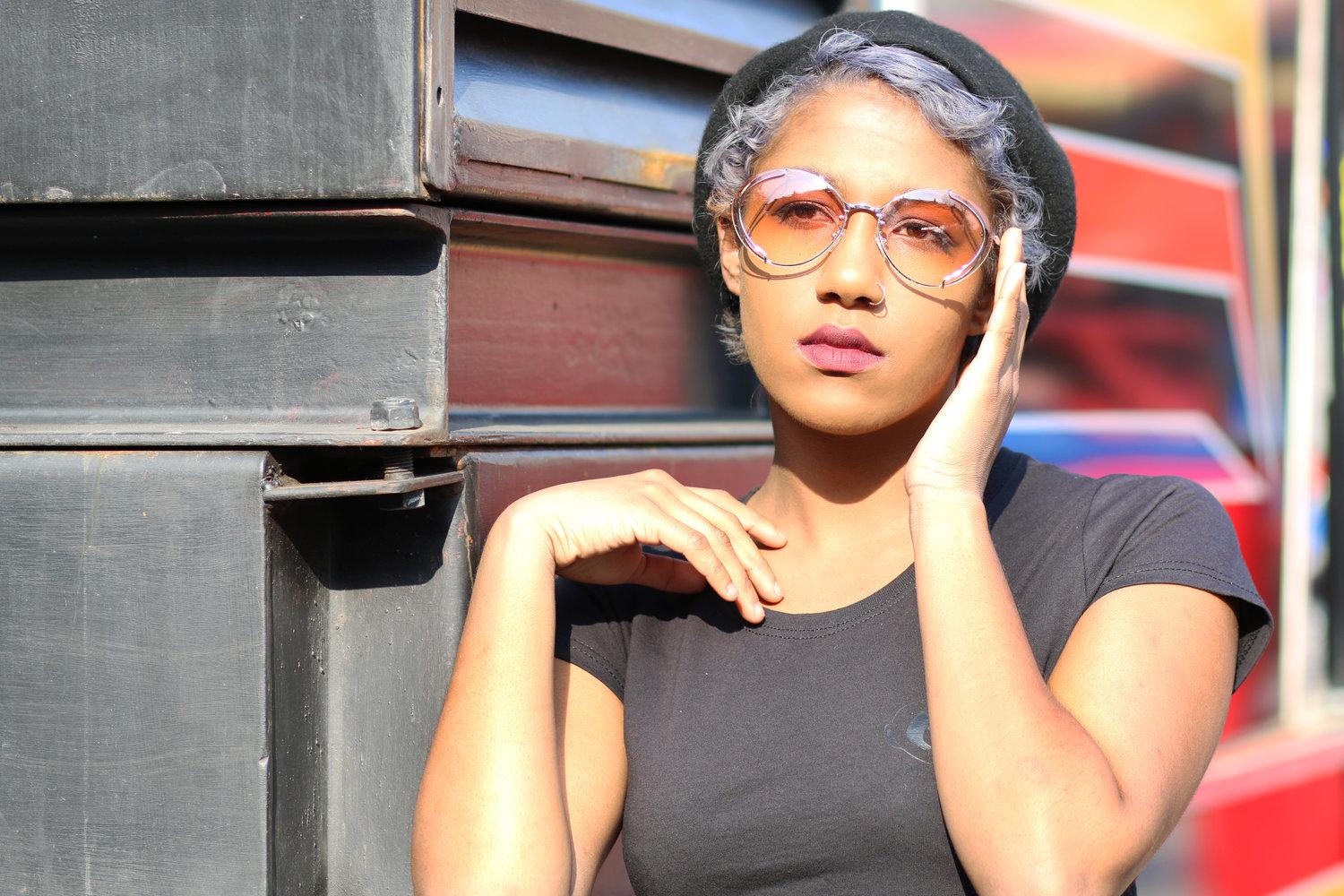 Rhyana with one hand on their cheek, dressed in black clothing.