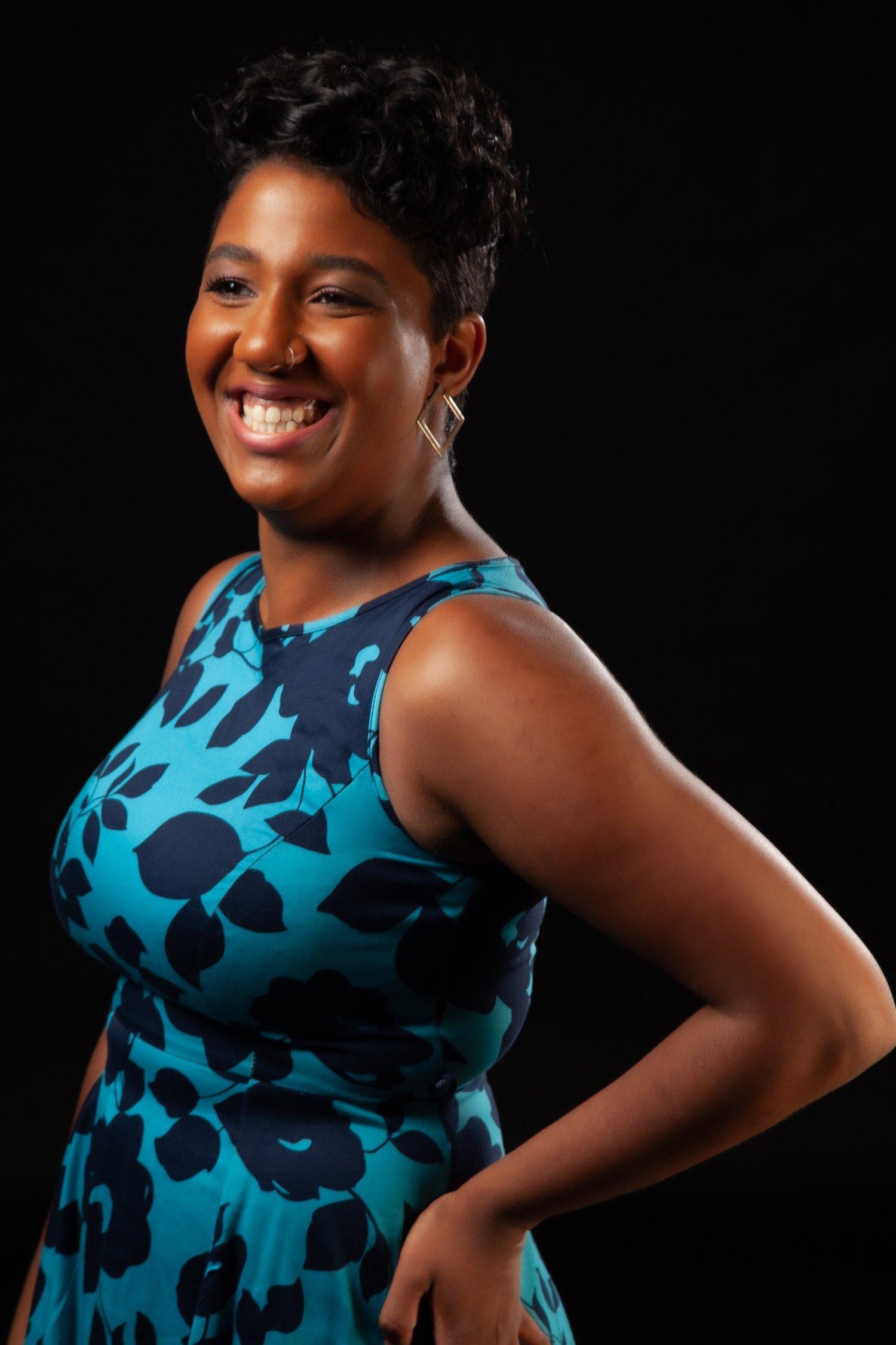 Rhyana smiling in a blue and black leaf-patterned dress.