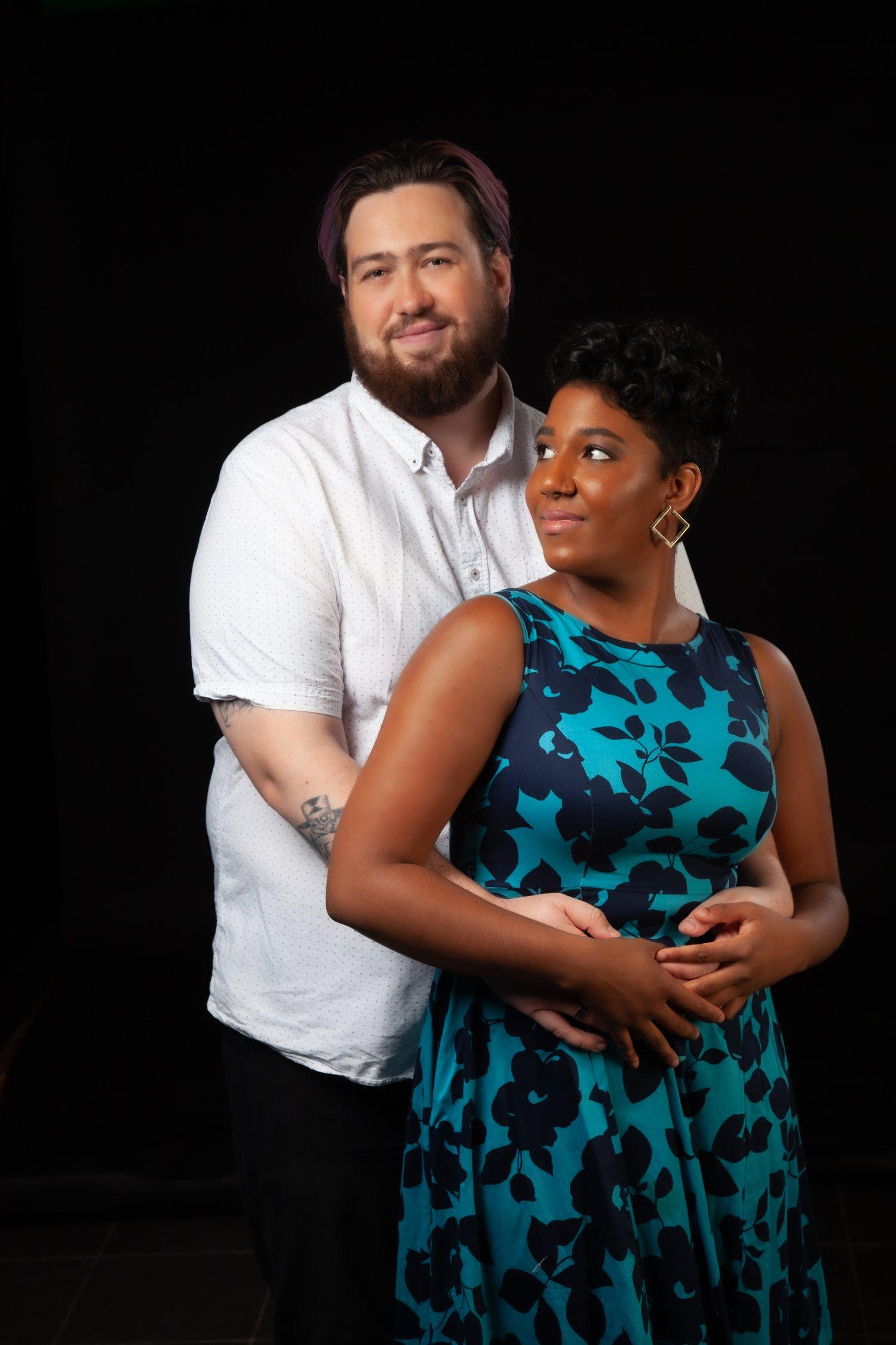 Rhyana in a blue and black floral dress, being embraced by partner Matt.