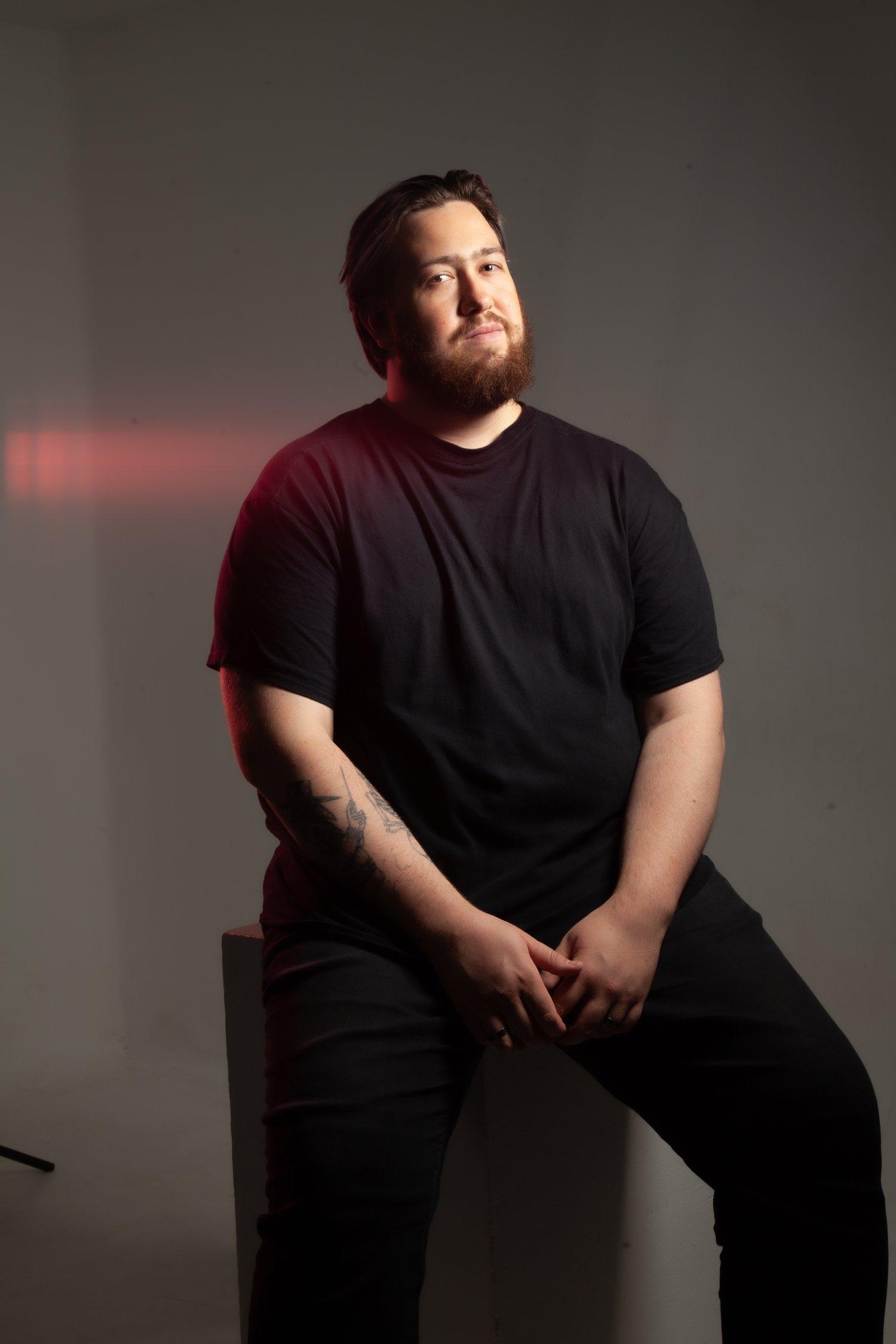 Matt looking towards the camera, sat in a black t-shirt and trousers.