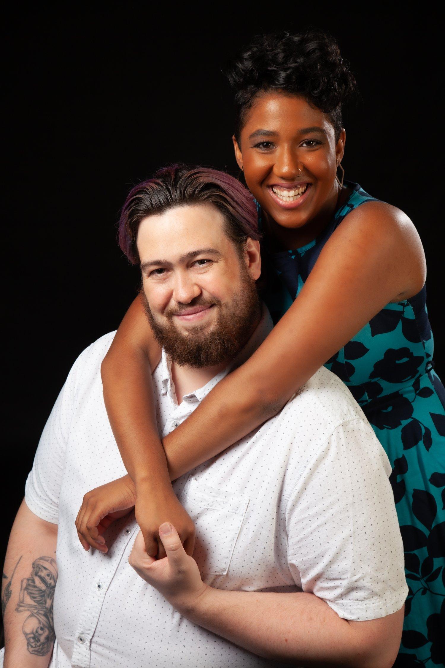 Matt in a white shirt, sat in front of Rhyana in a blue and black floral dress.