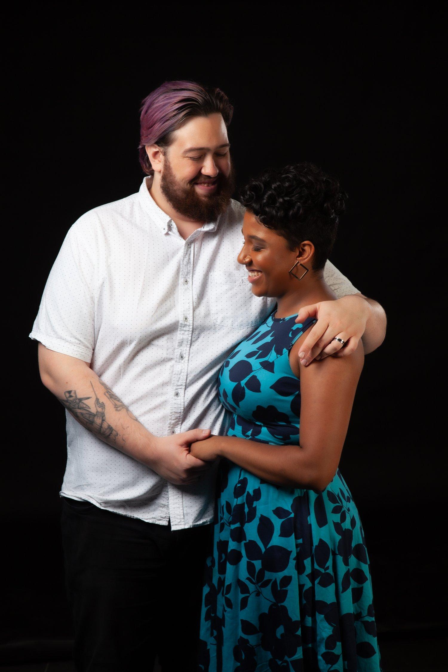 Rhyana in a blue and black floral dress, being embraced by partner Matt.
