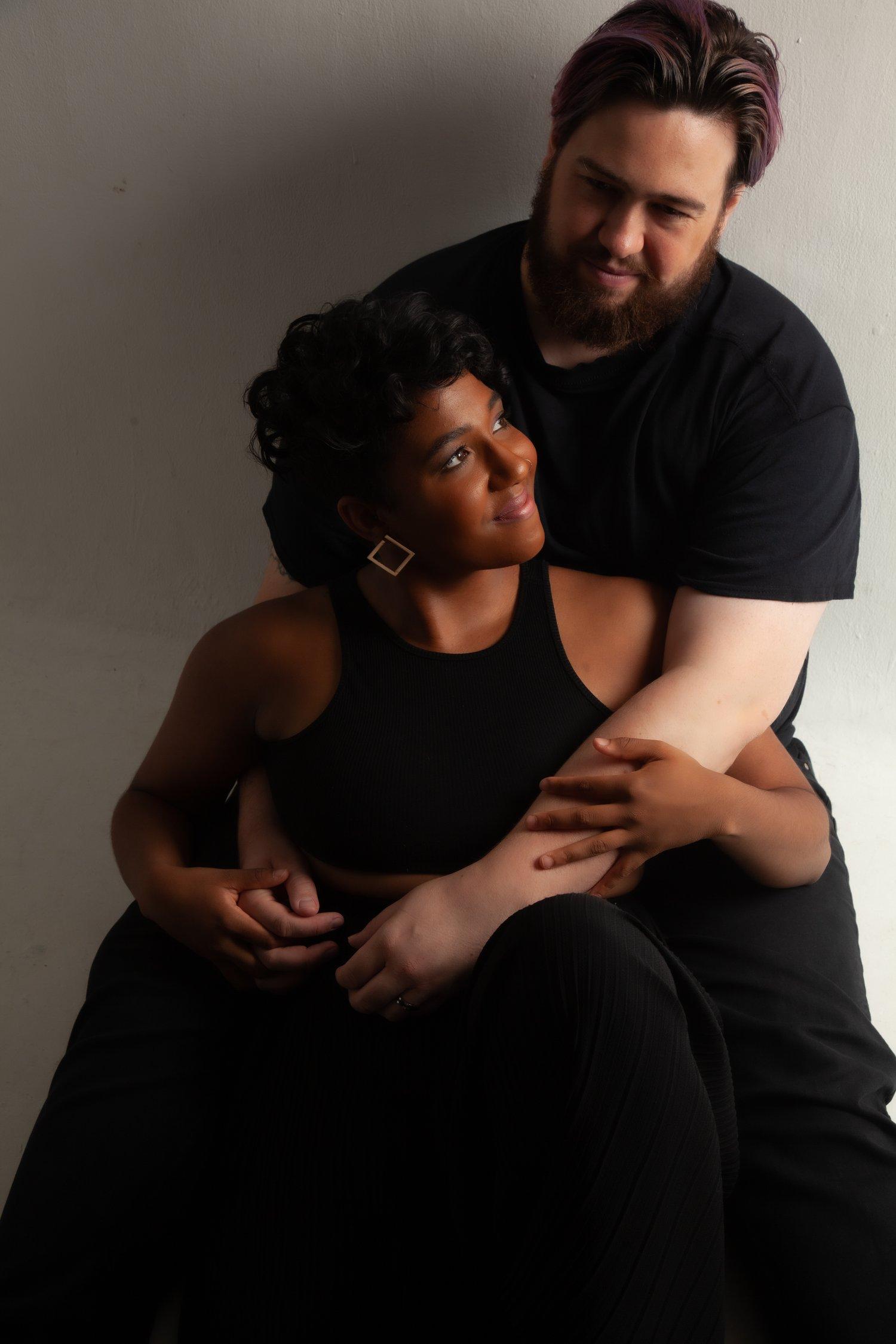 Rhyana sat in a black sleeveless top, being embraced by Matt, who wears a black t-shirt and trousers.