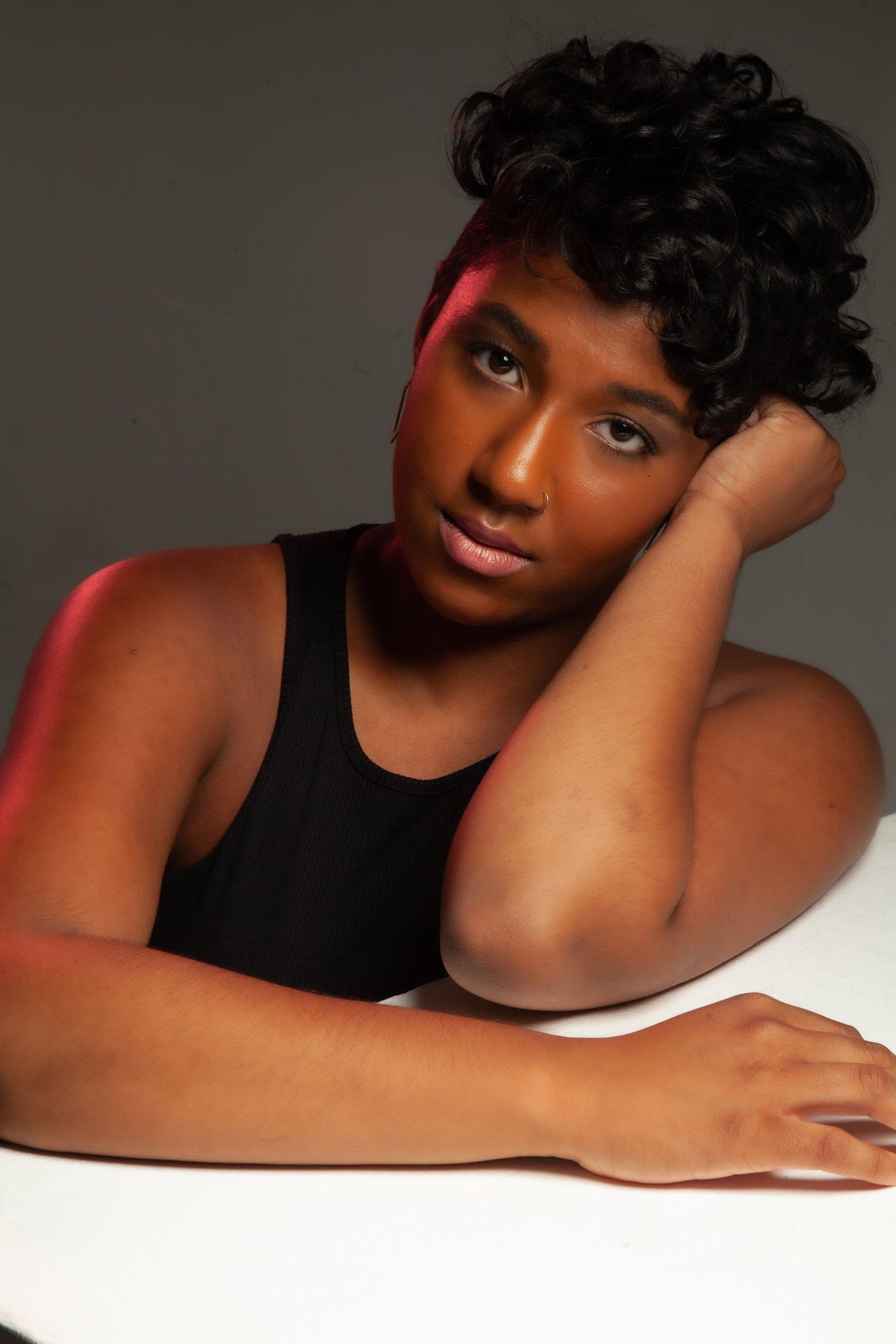 Rhyana leaning on one arm, looking towards the camera in a black sleeveless top.