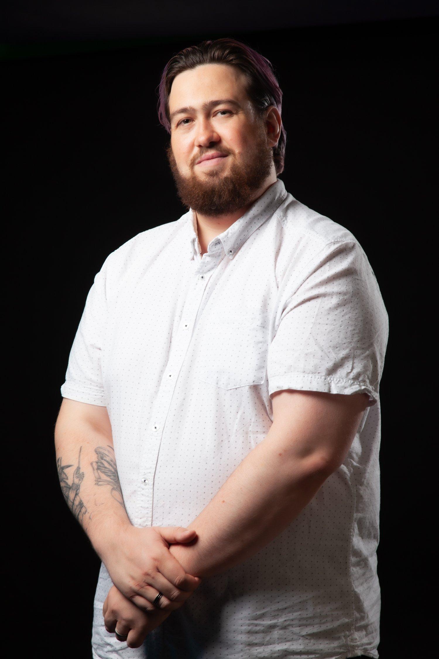 Matt with arms in front smiling towards the camera in a white shirt.
