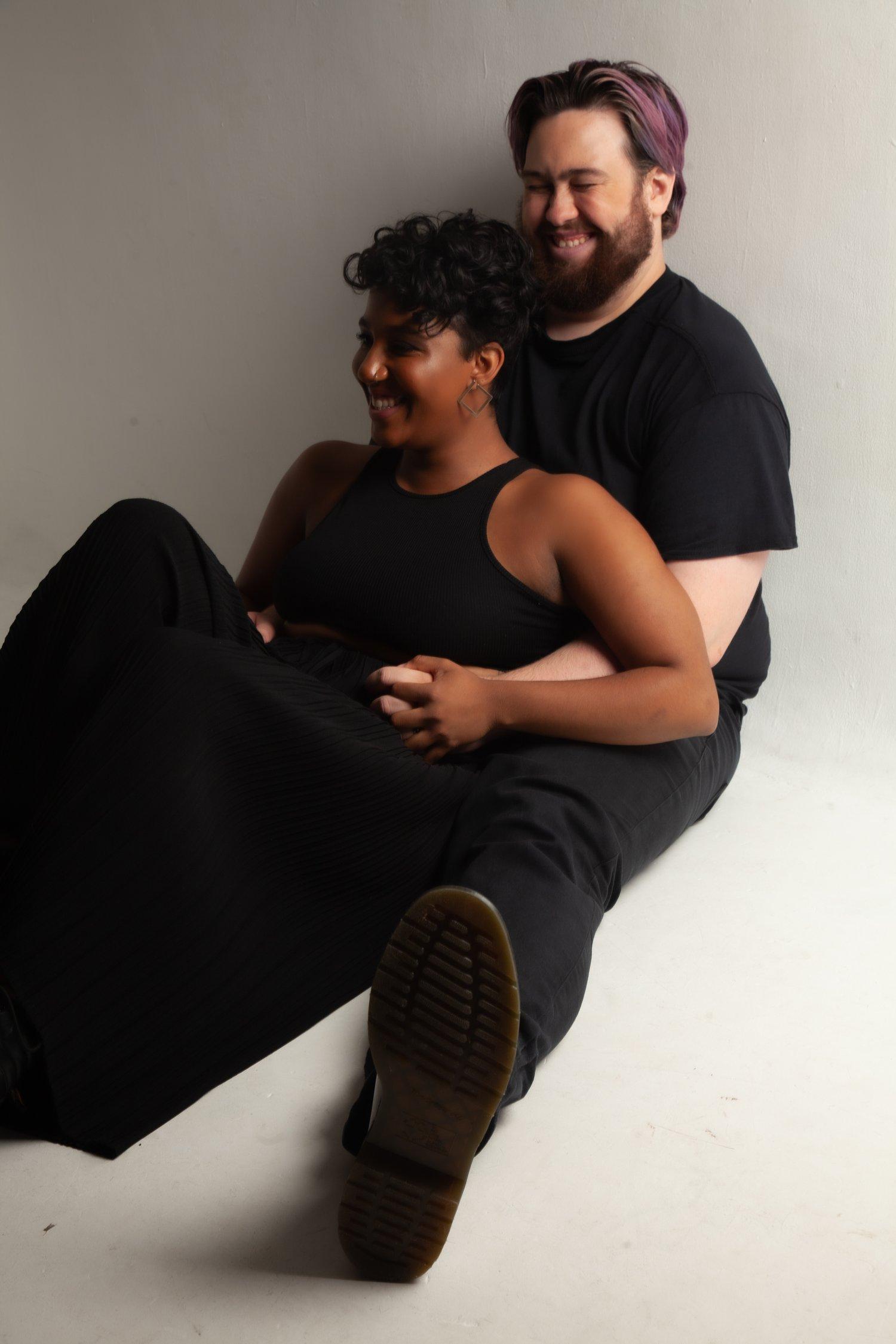 Matt and Rhyana sat against a white background, smiling as he embraces her.