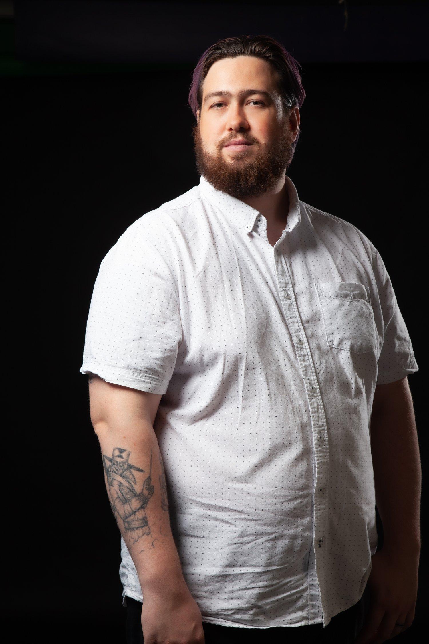 Matt stood with pink hair and wearing a white shirt against a black background.