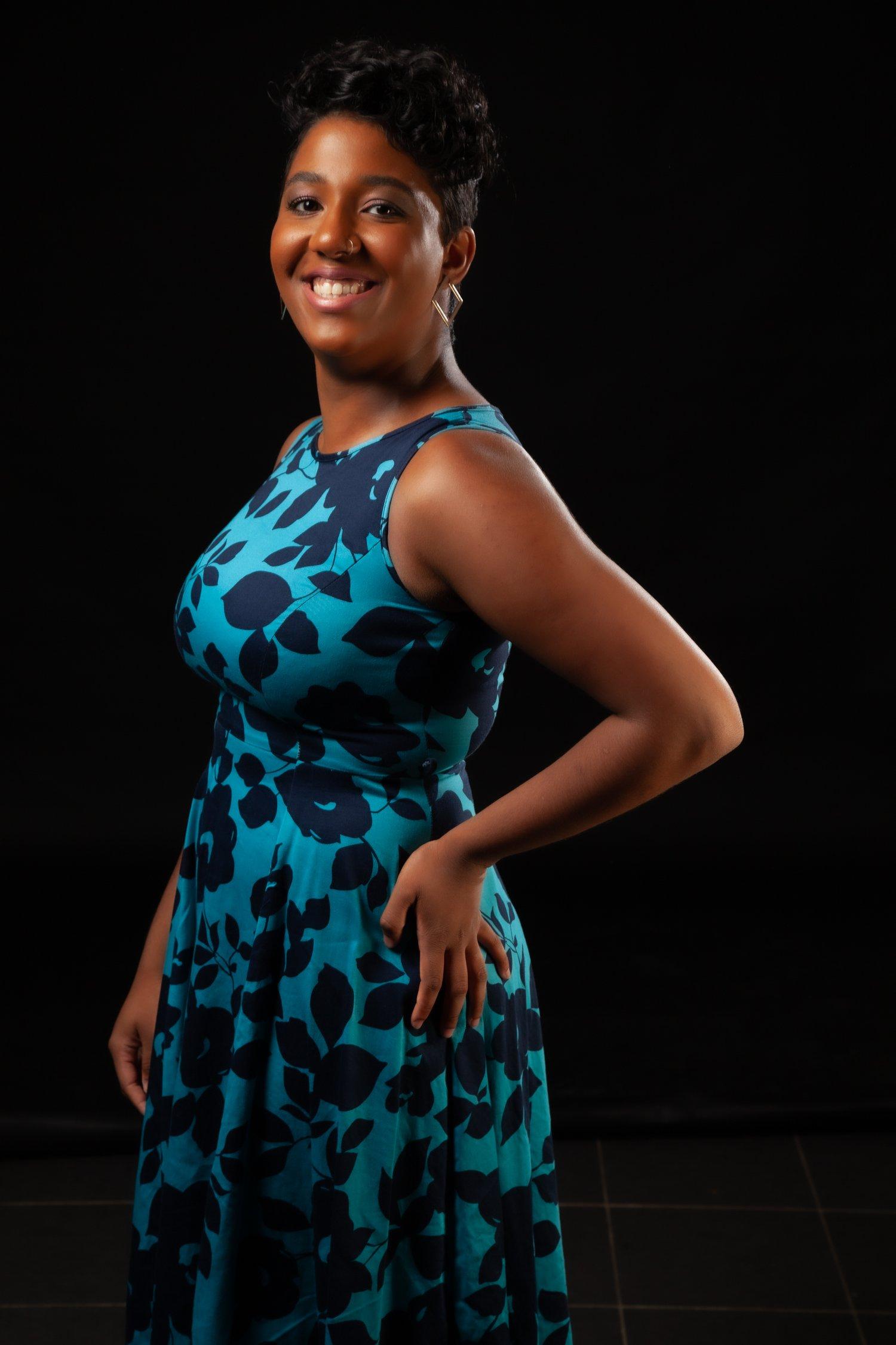 Rhyana smiling in a blue and black dress against a black background.
