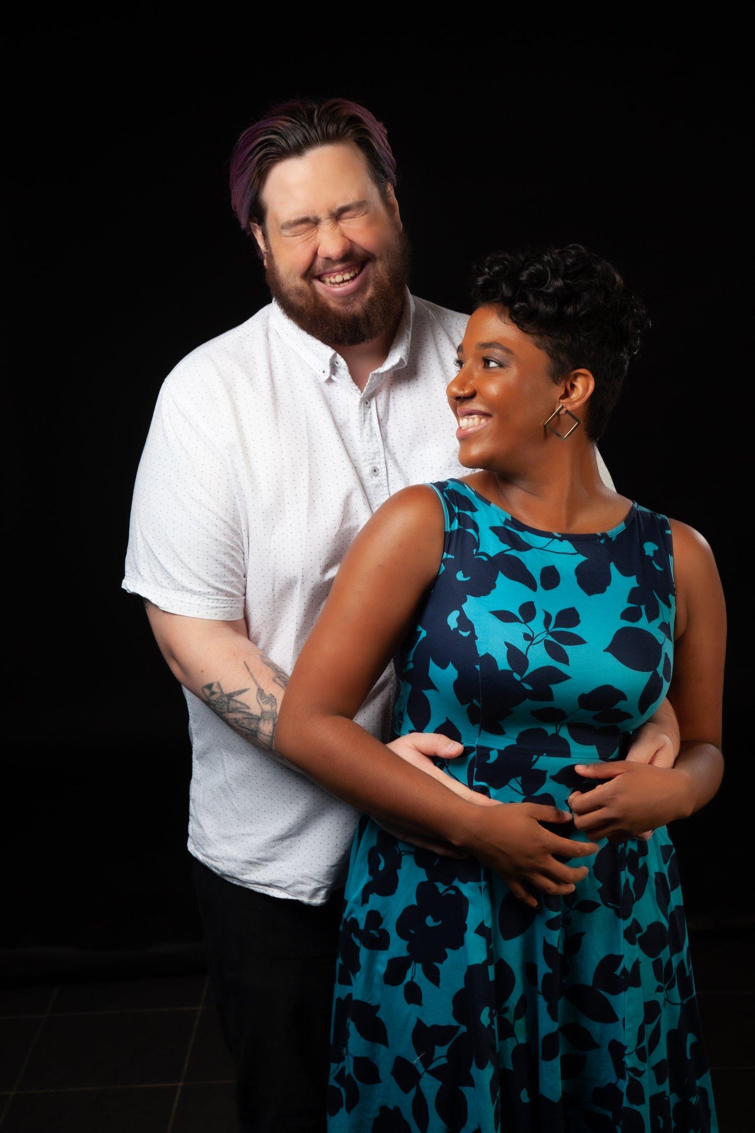 Rhyana smiling in a blue and black floral dress as Matt laughs and embraces her.