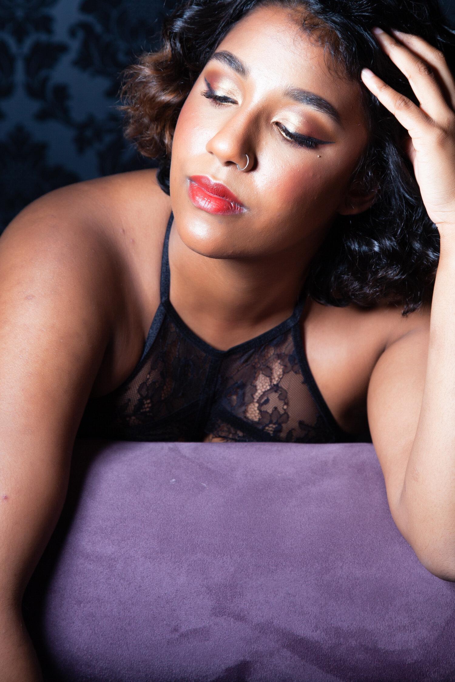 Rhyana in black lace lingerie with a hand on their head, looking downwards.
