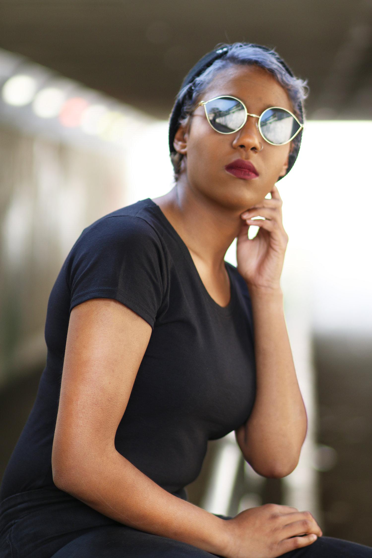 Rhyana leaning on one arm over a railing, wearing a dark blue t-shirt and looking towards the camera.