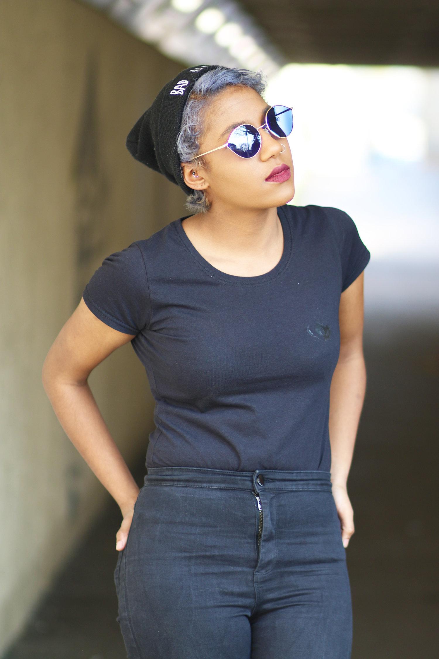 Rhyana with hands on their hips, wearing dark clothing and looking off-camera.