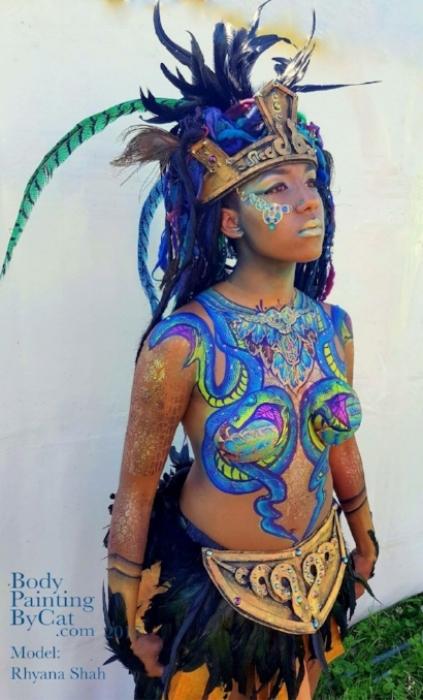 Rhyana in a golden warriors outfit with feathered headdress and snake-themed chest body art.