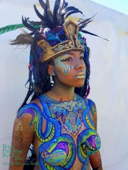Rhyana in golden, feathered headdress with snake-themed blue and green body art.
