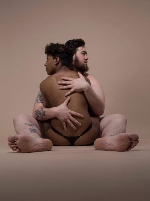 Rhyana and Matt embrace naked on the floor against a muted brown background.