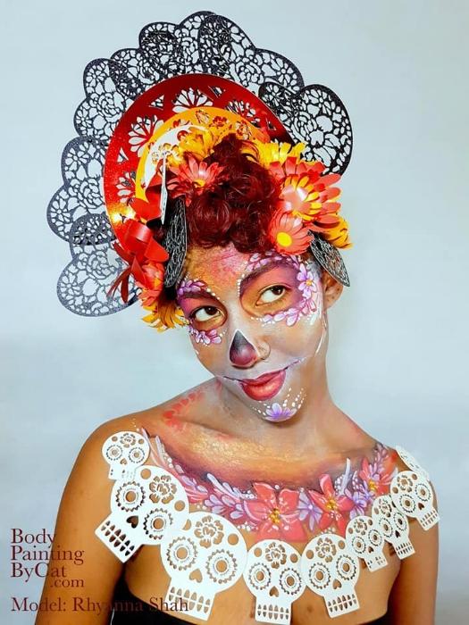 Rhyana dressed in black, white and red skull and flower motif outift, looking upwards off-camera.