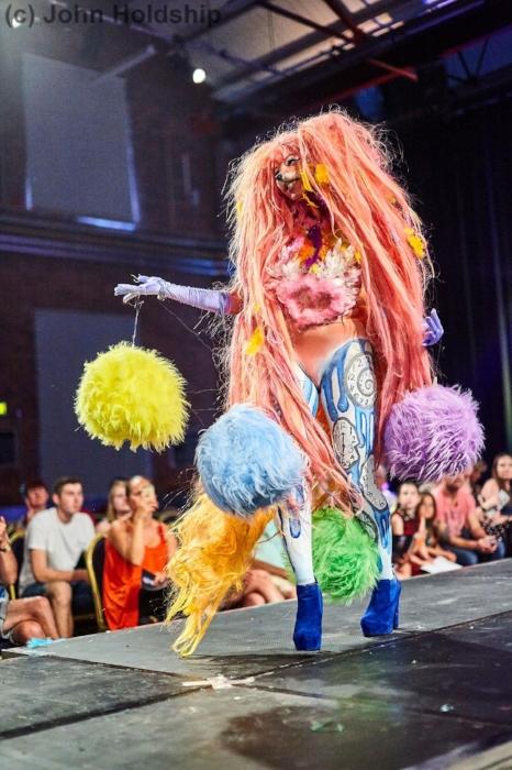Close up of Rhyana in a colourful fur fox outfit with blue heels, walking on a modelling catwalk.