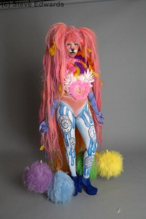 Rhyana standing against a white background in a fur fox outfit with colourful fur tassles.