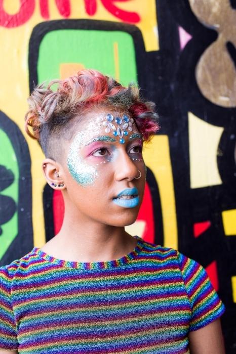 Close up of Rhyana posing in a multi-colored striped shirt with blue and pink makeup.