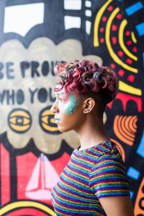 Rhyana in profile, wearing a multi-colored striped shirt and blue makeup.