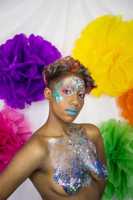 Rhyana posing topless in silver and blue bodypaint with matching makeup, looking towards camera.