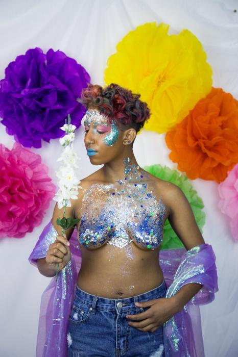 Rhyana holding a tall, white flower, dressed in denim shorts and silver / blue bodypaint.