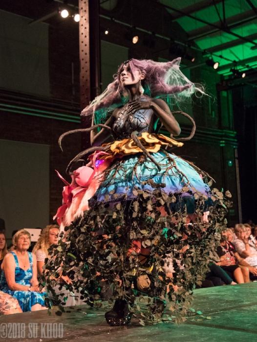 Rhyana in a forest-themed outfit with long claws, walking on a modelling catwalk.