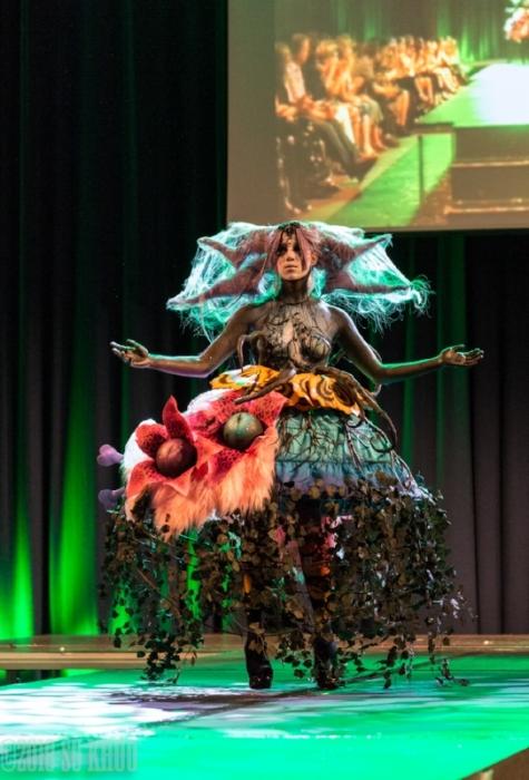 Rhyana with arms outstretched arms in a forest-themed outfit on a modelling catwalk.