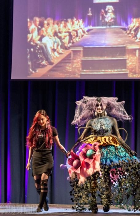 Rhyana smiling in a forest-themed outfit against a purple background with designer Tawna Lee.
