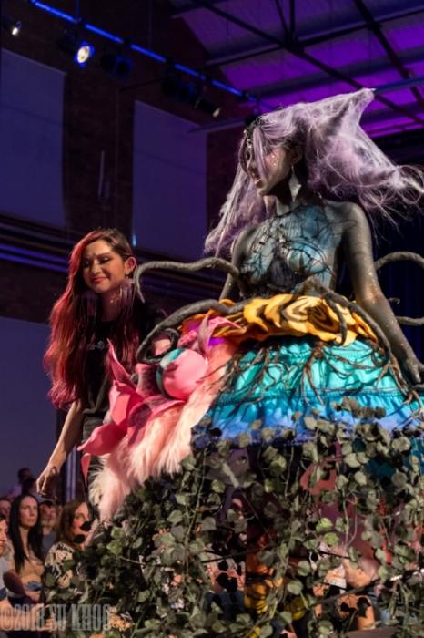 Rhyana  in a forest-themed outfit with designer Tawna Lee on a purple-lit modelling catwalk.