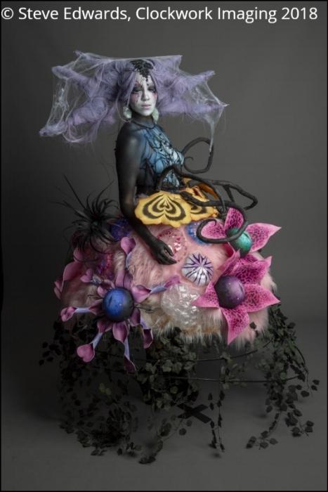 Long shot of Rhyana in a forest-themed outfit against a grey background.