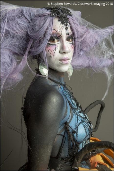 Close up of Rhyana in a forest-themed outfit and makeup against a grey background.