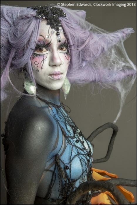 Close up of Rhyana in a forest-themed outfit with long claws against a grey background.