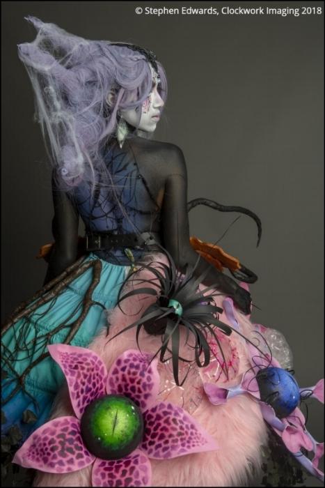 Rhyana in a spooky forest-themed outfit looking off camera against a grey background.