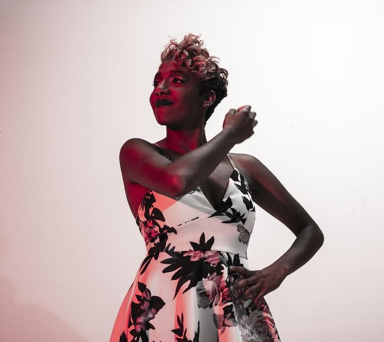 Rhyana in a white floral dress looking off camera in dark red lighting.
