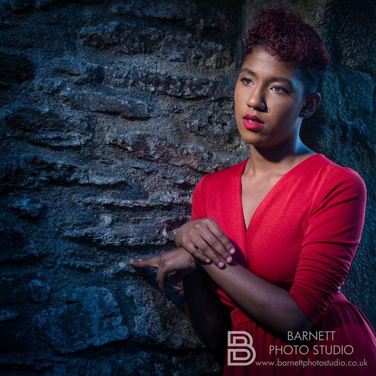Rhyana posing against a cobbled brick wall in a red dress.
