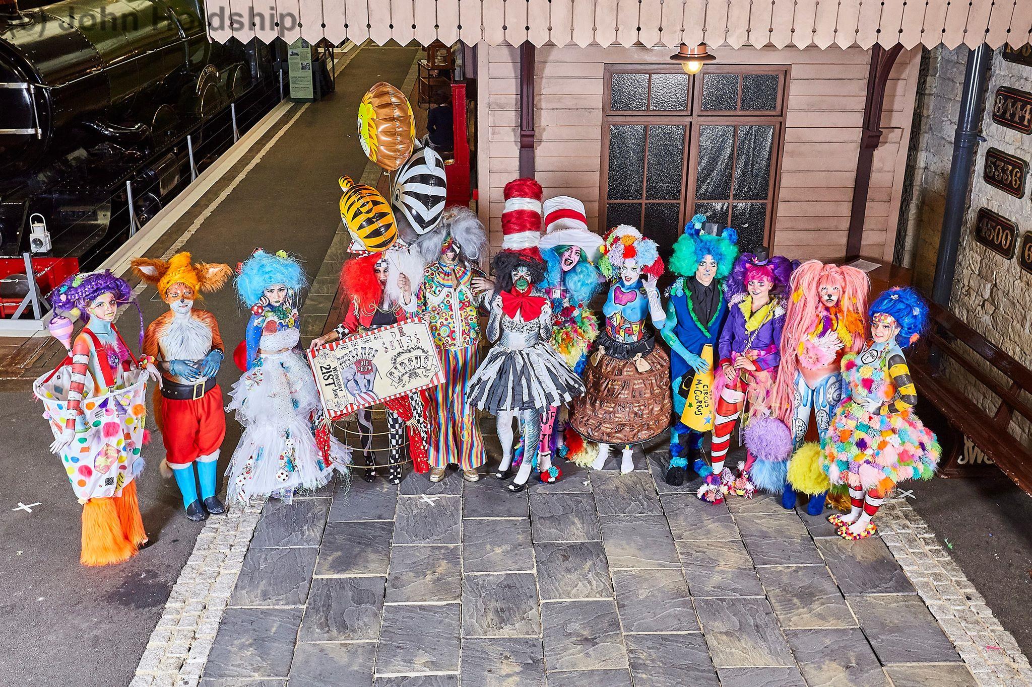 Rhyana in a colourful fox costume together with a variety of other characters standing on a cobbled street.